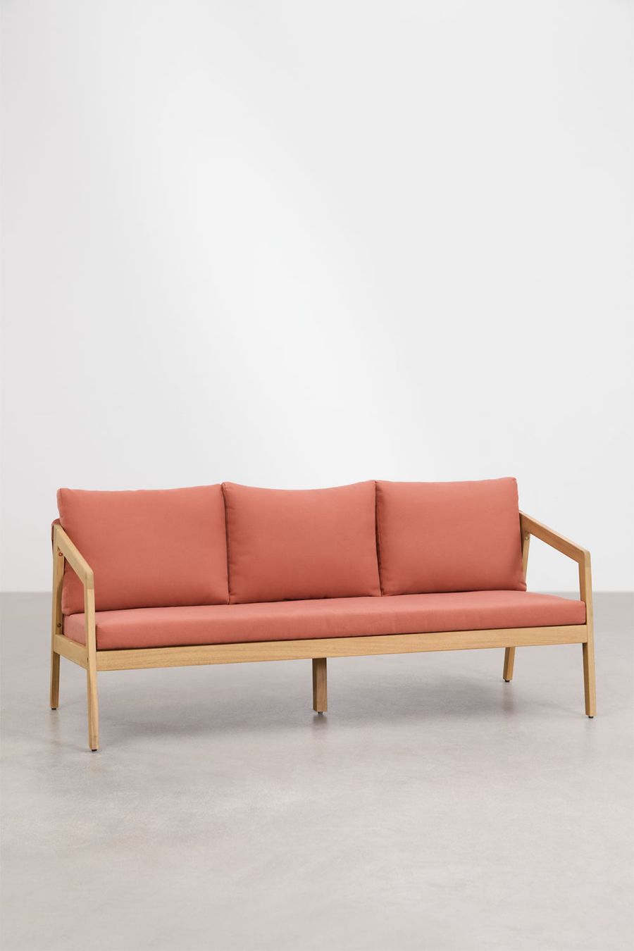Canapé Kaela en bois clair et tissu terracotta, vu de face dans une pièce blanche au sol gris.