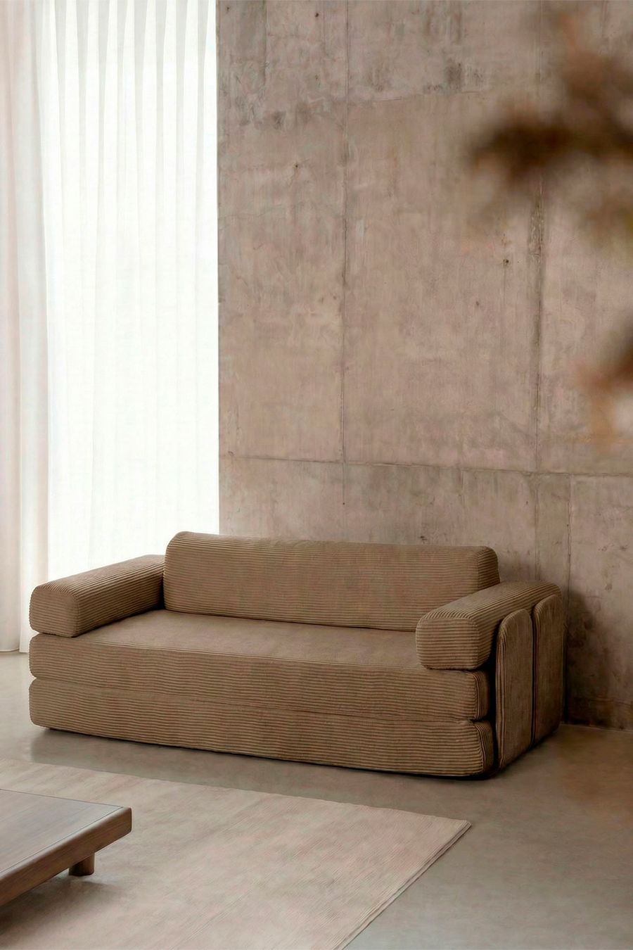 Canapé Paoly en velours côtelé marron taupe vu de trois quarts, contre un mur en béton, dans un salon.