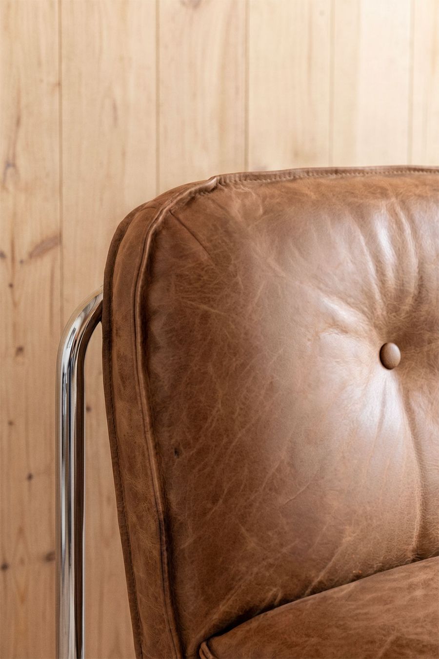 Gros plan du cuir marron du canapé Matilda, avec un bouton de capiton et l'accoudoir chromé.