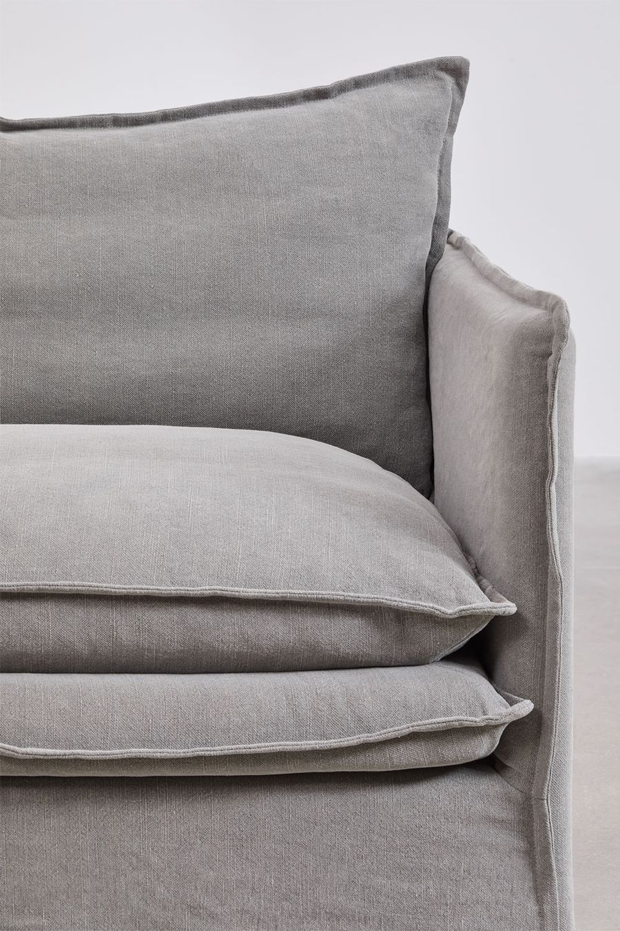 Gros plan sur un coussin d'assise et l'accoudoir du canapé Grace en tissu gris.