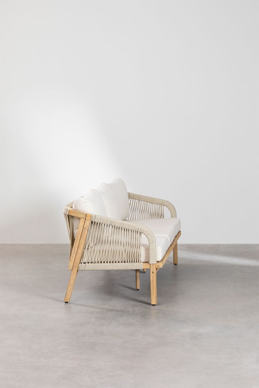 Canapé Dubai vu de trois quarts, accoudoir en cordage beige et pieds en bois, sur sol béton.