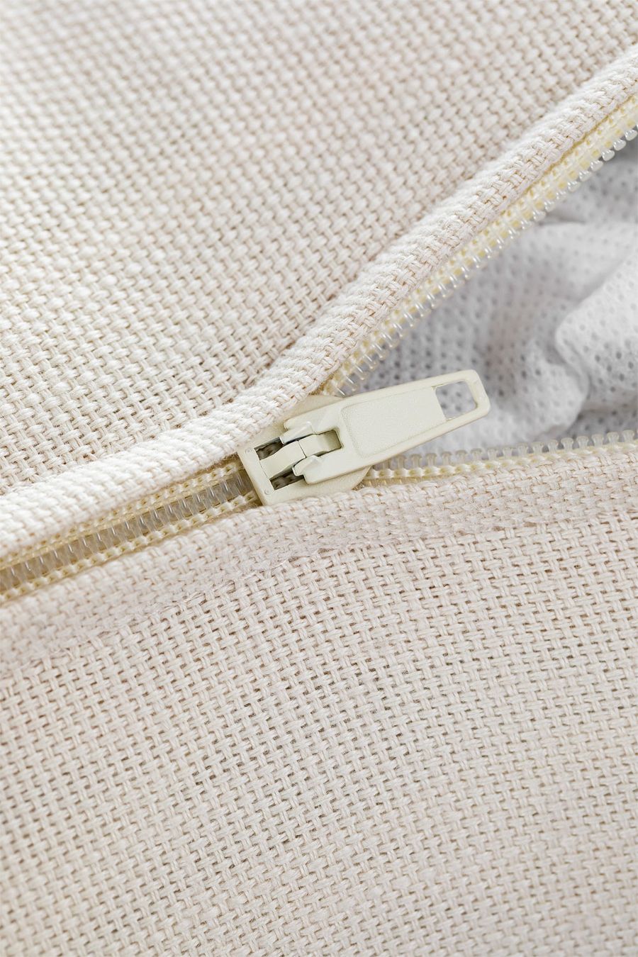 Gros plan d'une fermeture éclair blanche sur un tissu de coussin beige clair.