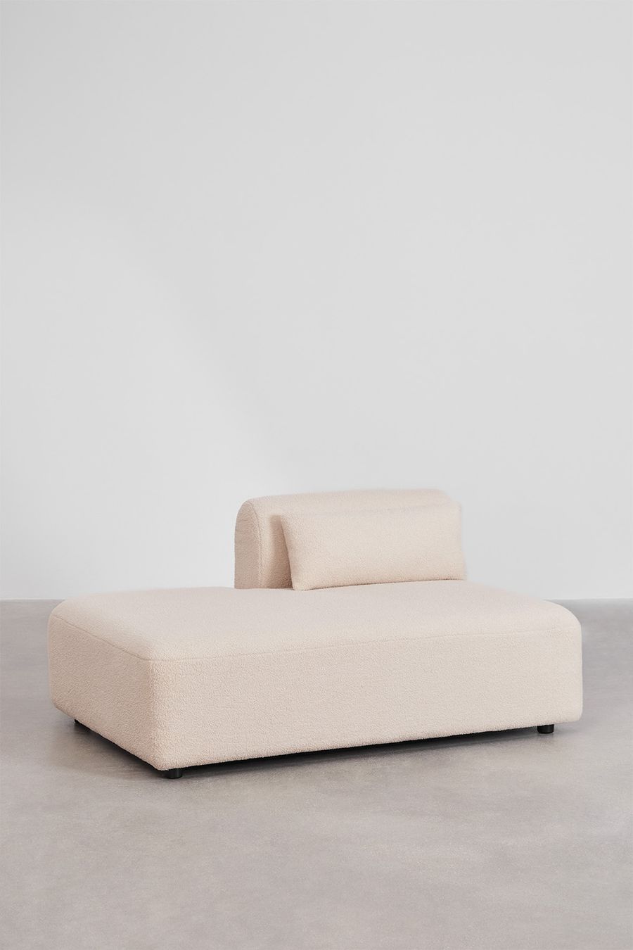 Module méridienne du canapé Fogler en tissu bouclé beige, avec un coussin de dossier, sur sol gris.