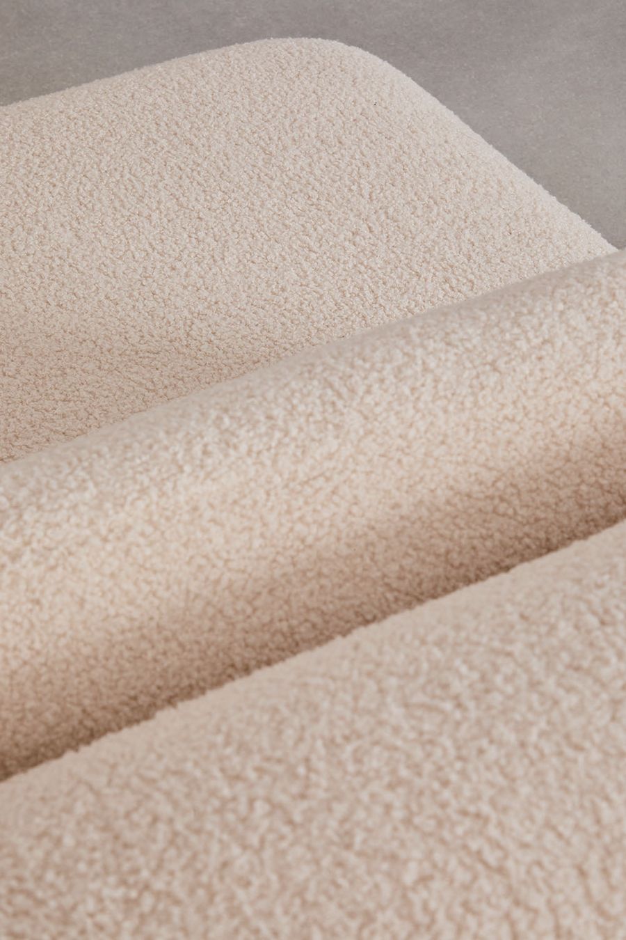 Gros plan du tissu bouclé beige crème du canapé Fogler, aux surfaces arrondies.