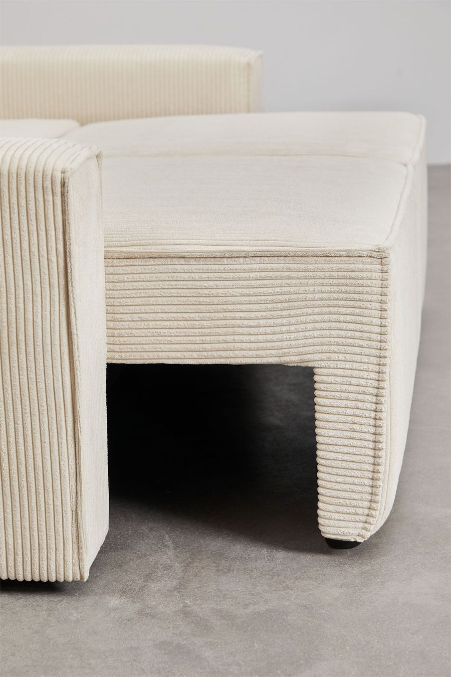 Gros plan du coffre bas et des pieds du canapé Tampere en velours côtelé beige crème.