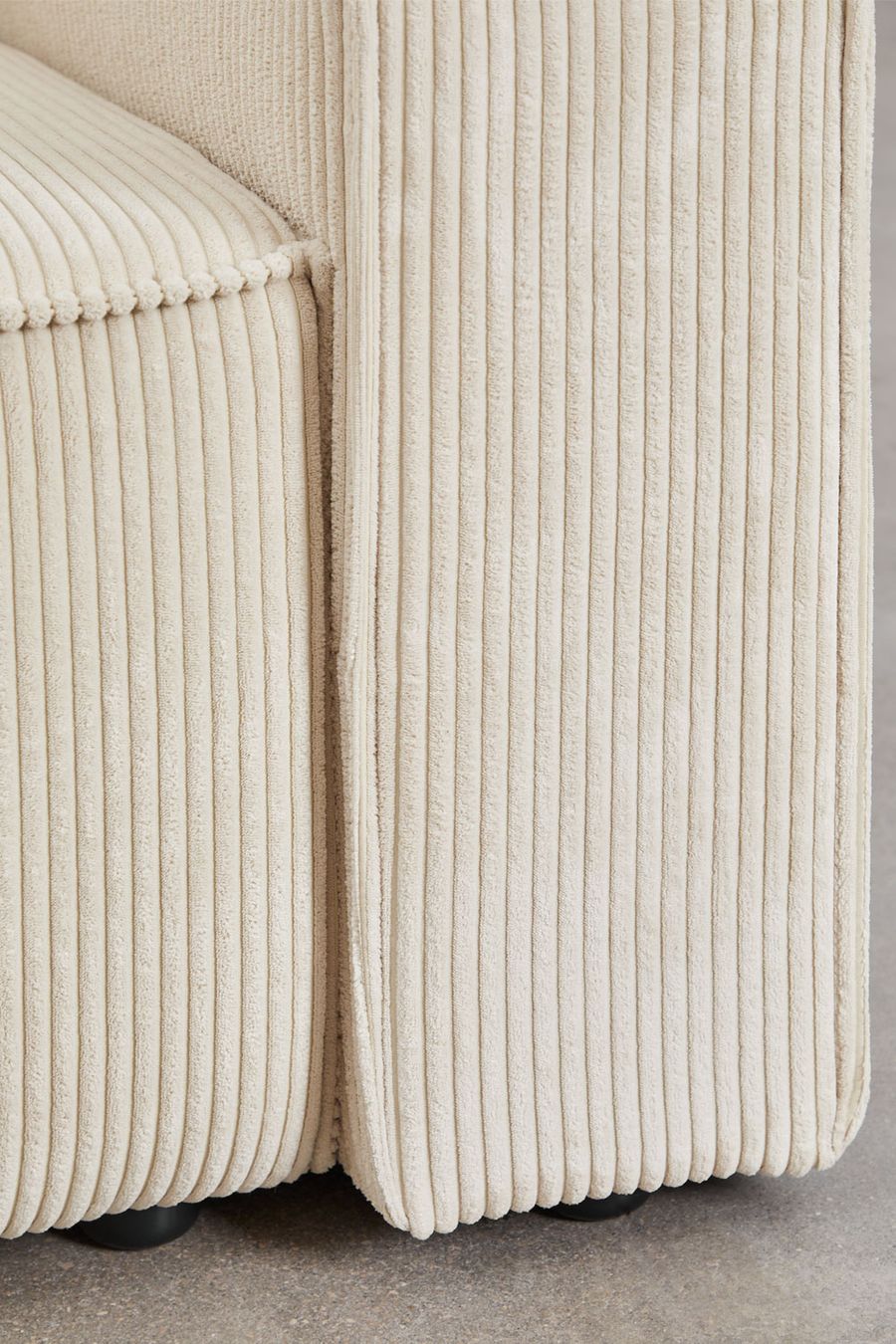 Gros plan des accoudoirs et des pieds noirs du canapé Tampere en velours côtelé beige crème.