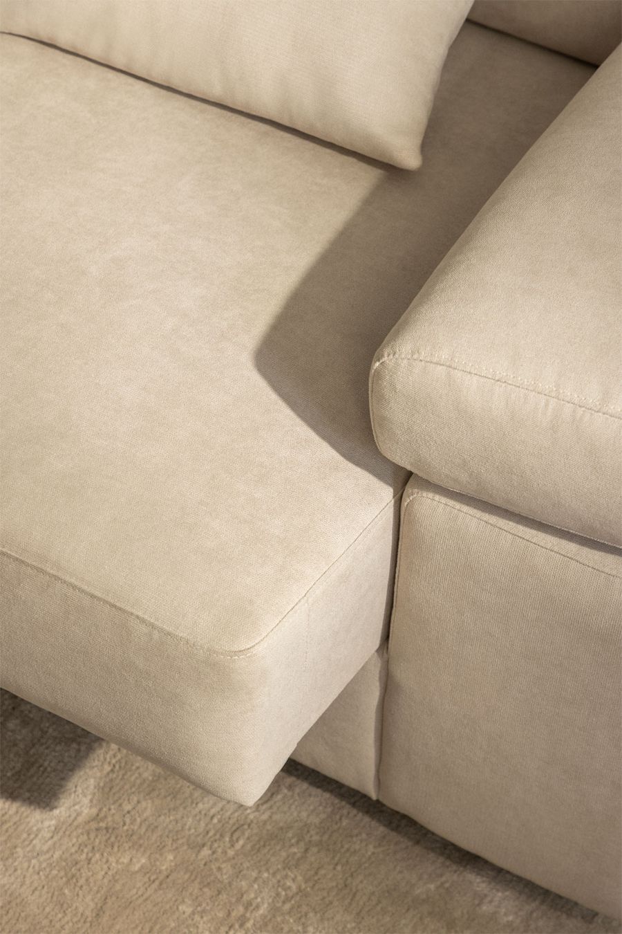 Gros plan de l'assise de la méridienne et de l'accoudoir arrondi du canapé beige.