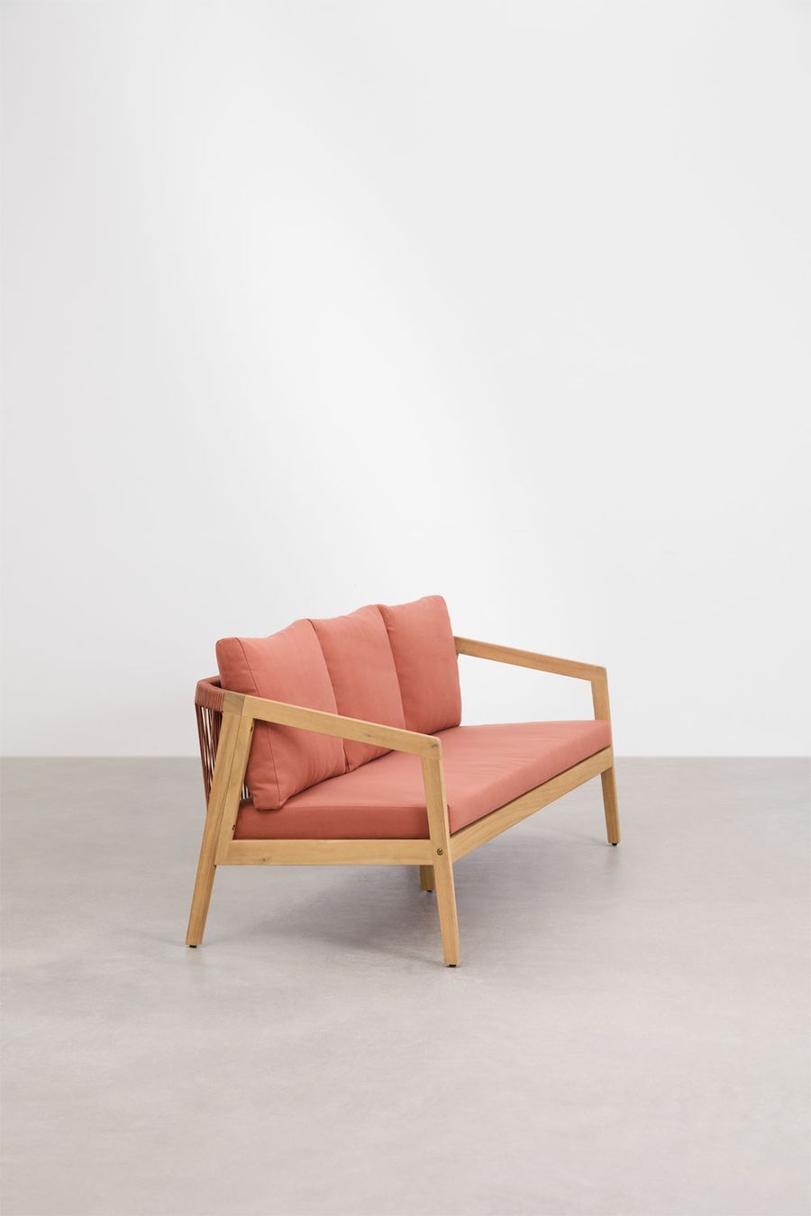Canapé Kaela en bois clair et tissu terracotta, vu de trois quarts sur sol gris, mur blanc.