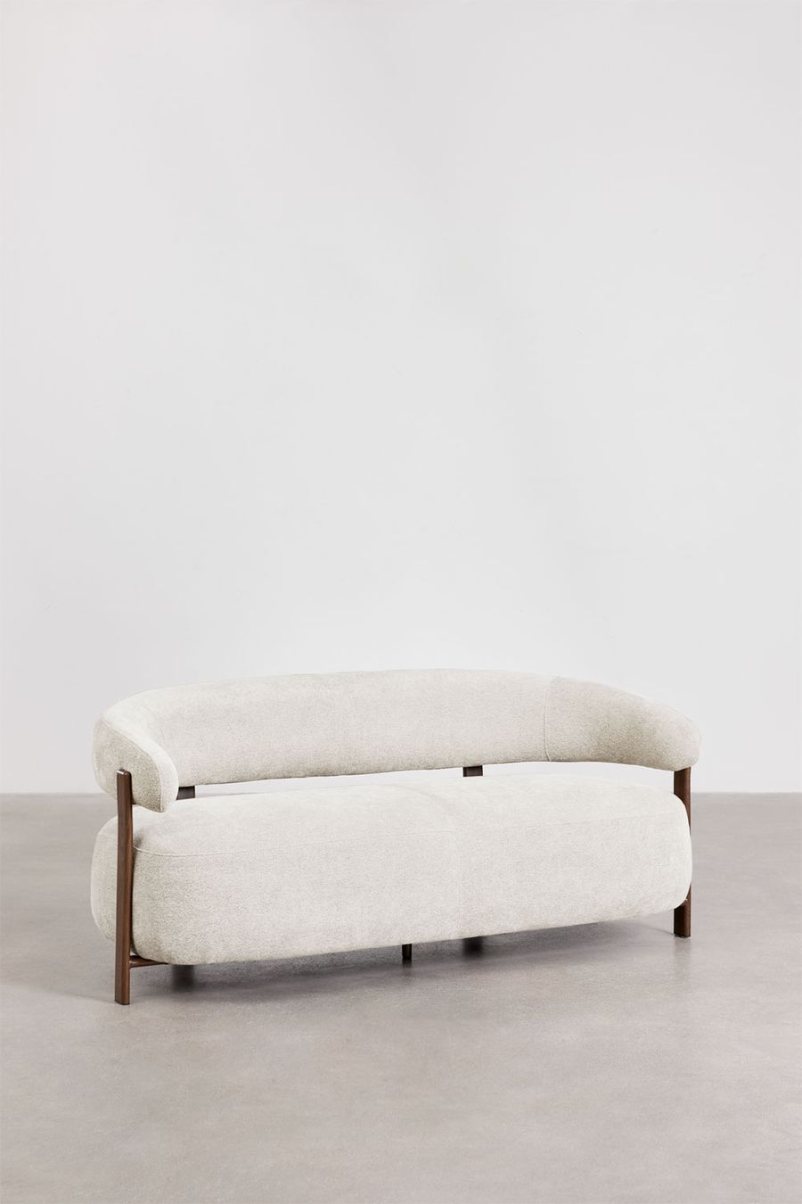 Canapé Jolie en tissu chenille crème vu de trois quarts, pieds en bois foncé, sur sol béton clair.