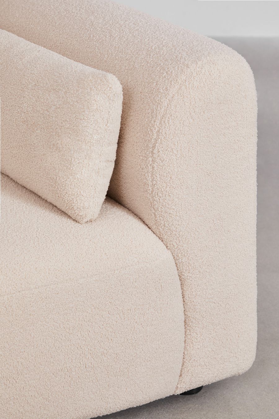 Gros plan de l'accoudoir arrondi et du coussin de dossier du canapé Fogler en tissu bouclé beige.