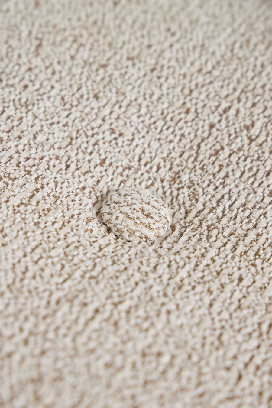 Gros plan d'un bouclé beige chiné avec un bouton de capiton au centre.
