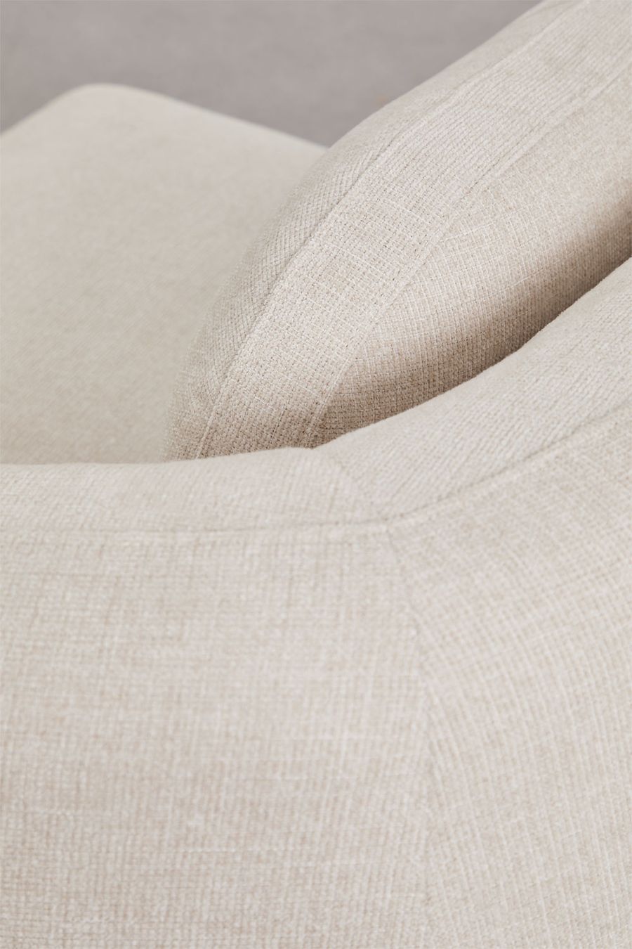Gros plan de la couture et de l'accoudoir arrondi du canapé Coquette en tissu beige.