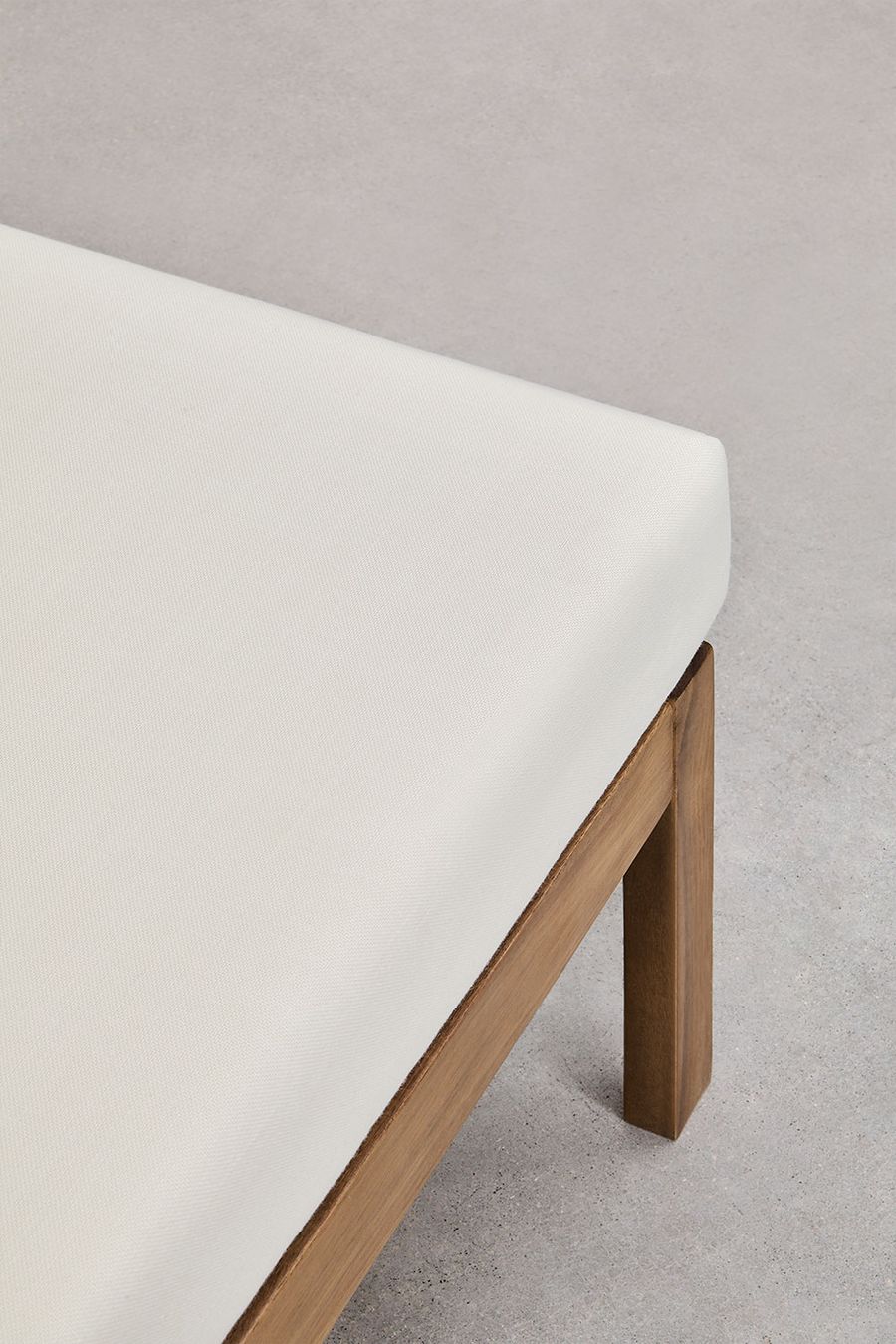 Gros plan d'un coin de l'assise crème et d'un pied en bois d'acacia du canapé Branson.