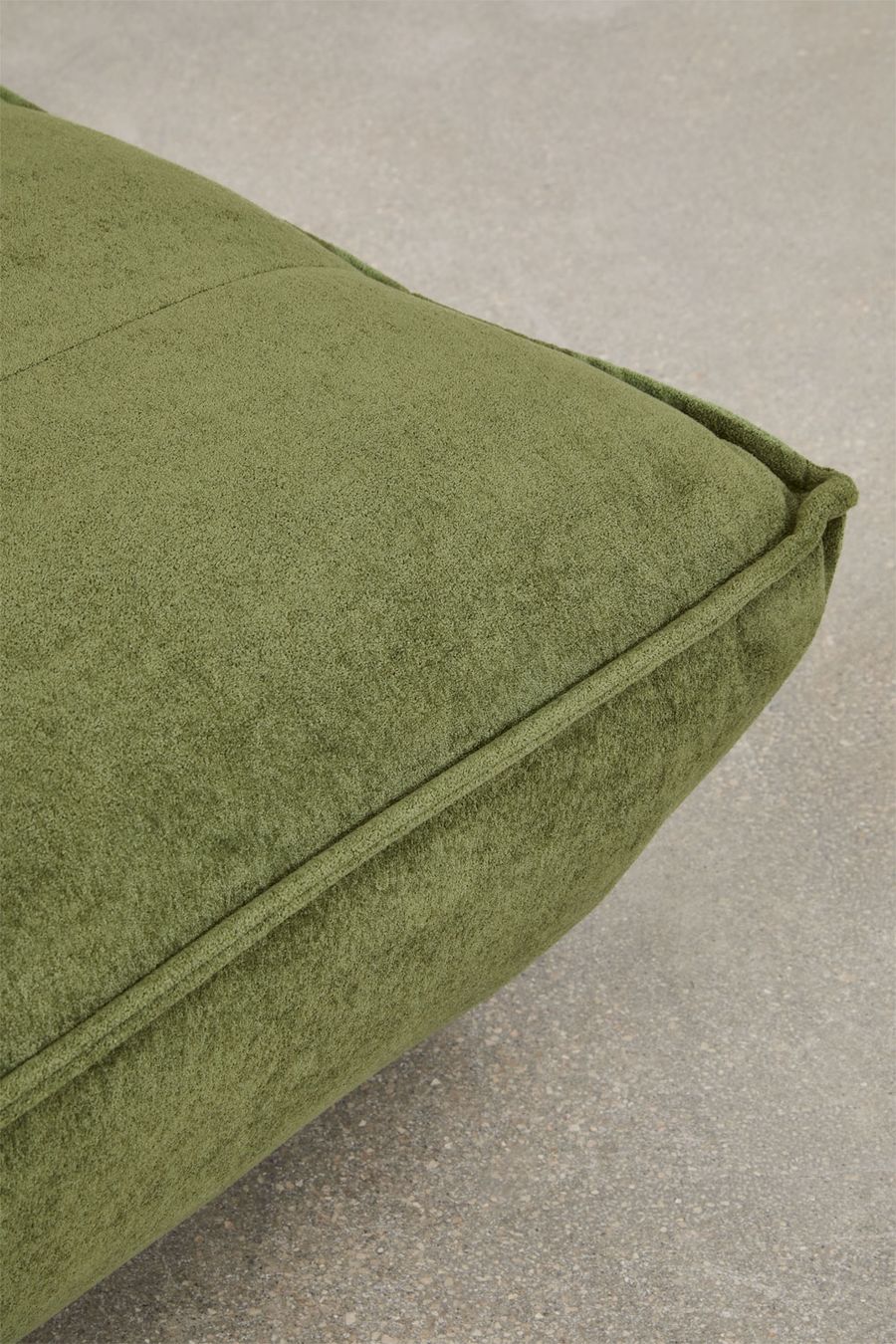 Gros plan d'un angle d'assise du canapé Mati en tissu vert avec passepoil.