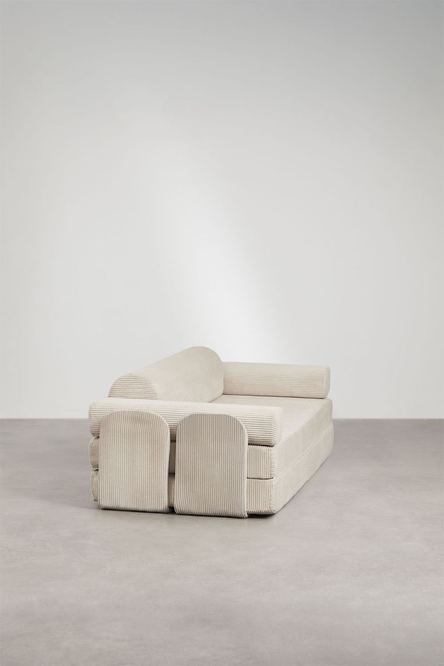 Canapé Paoly beige vu de trois quarts arrière, accoudoirs et modules arrondis visibles, sur sol gris.