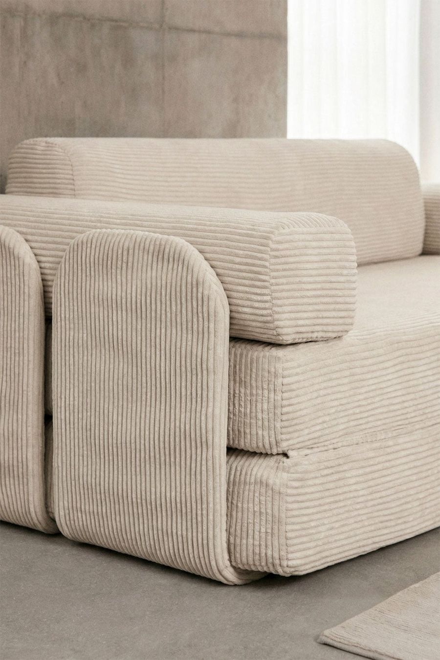 Gros plan du velours côtelé beige du canapé Paoly, de son accoudoir arrondi et de ses coussins.