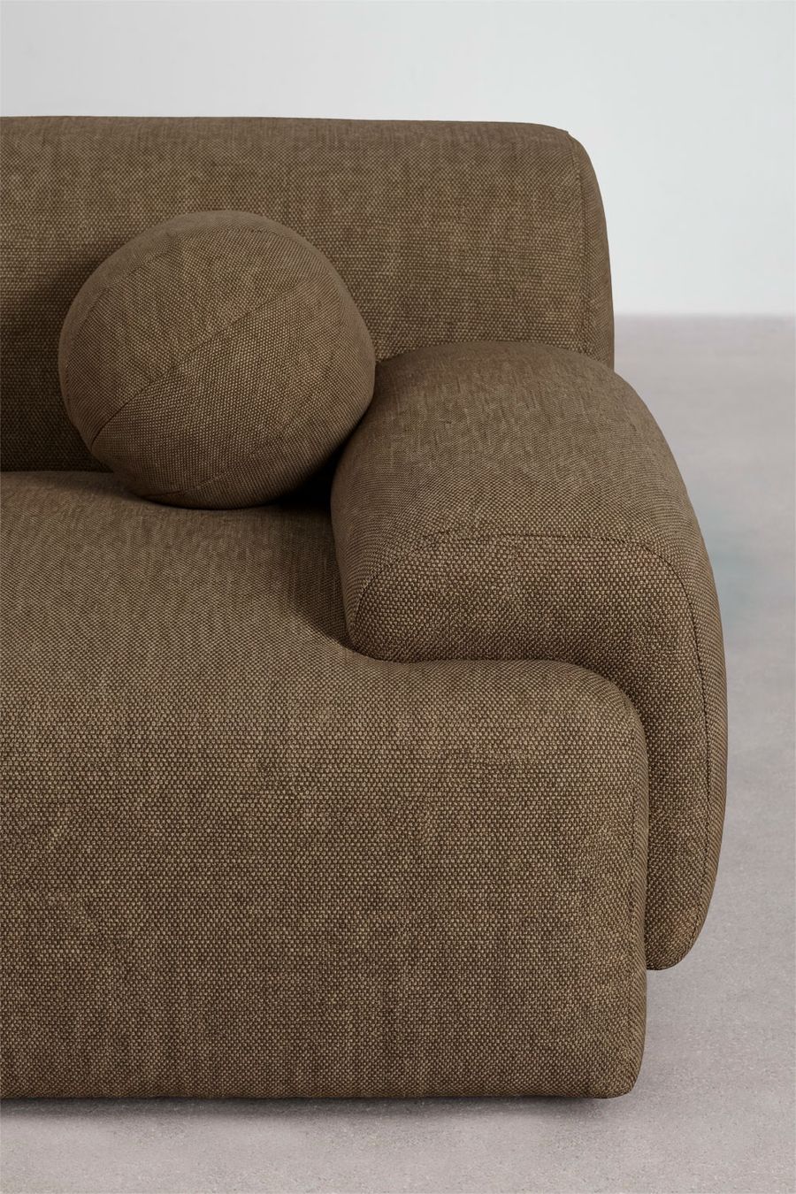 Gros plan d'un coussin boule et de l'accoudoir du canapé en tissu brun chiné texturé.