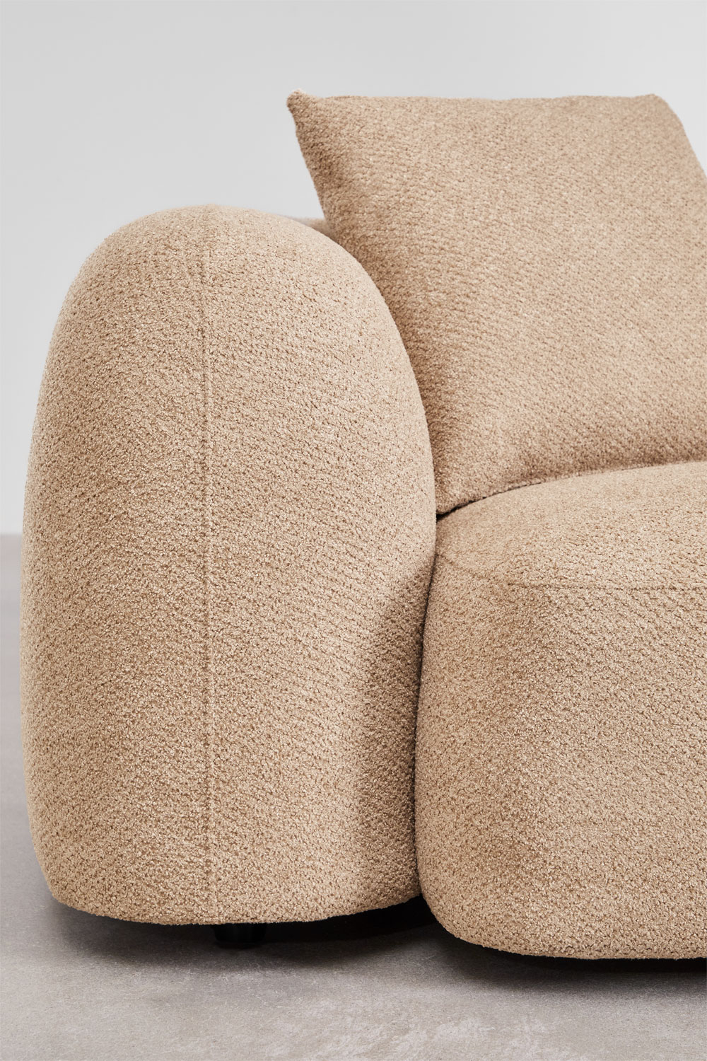 Gros plan de l'accoudoir arrondi et du dossier du canapé Coco en chenille beige.